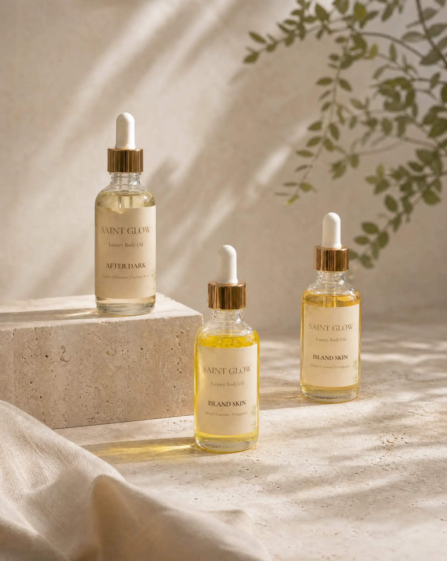 Three Saint Glow body oil bottles — After Dark and Island Skin — styled on travertine in warm light